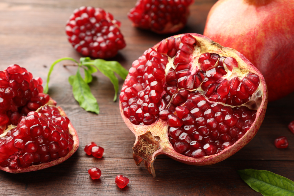 Cut fresh pomegranate and green leaves on wooden table